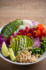 Vegetarian healthy food: quinoa, avocado, pomegranate, tomatoes, green peas, radish, red cabbage and lime salad in bowl on wooden table. vertical