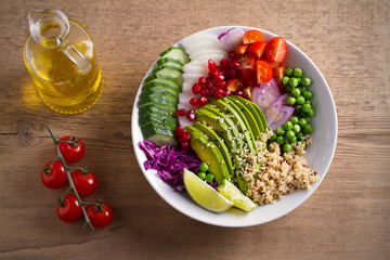 Vegetarian healthy food: quinoa, avocado, pomegranate, tomatoes, green peas, radish, red cabbage and lime salad in bowl on wooden table. overhead, horizontal
