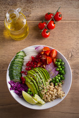 Vegetarian healthy food: quinoa, avocado, pomegranate, tomatoes, green peas, radish, red cabbage and lime salad in bowl on wooden table. overhead, vertical