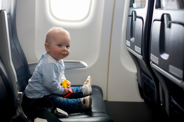 Cute baby boy, playing with toys on board of aircraft, traveling with parents and siblings