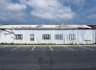 a row of dilapidated abandoned white tin sheet corrugated buildings with empty car park and blue sky and clouds