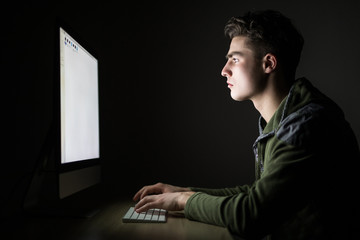 Focused handsome young man using computer in dark room at home