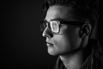 Close up of man face. Eyes of serious young man in black rim glasses using his tablet computer. Screen and finger reflecting in the glass. Gray photo.