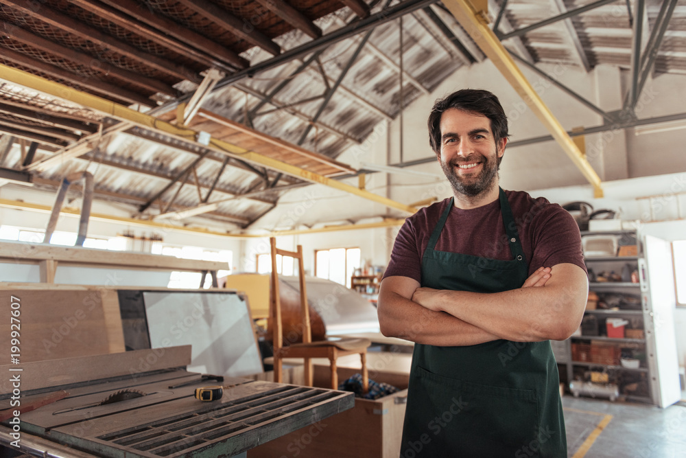 Wall mural smiling woodworker standing in his workshop by a bench saw