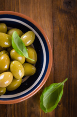 Green olives in a ceramic bowl on wooden background