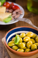 Green olives in a ceramic bowl on wooden background