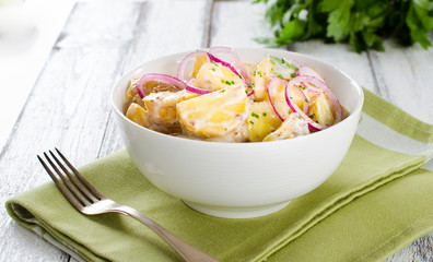 Fresh potato salad with mayonnaise dressing, onion and capers on white wooden background