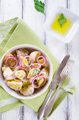 Fresh potato salad with mayonnaise dressing, onion and capers on white wooden background