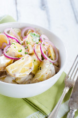 Fresh potato salad with mayonnaise dressing, onion and capers on white wooden background