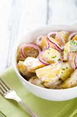Fresh potato salad with mayonnaise dressing, onion and capers on white wooden background