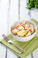 Fresh potato salad with mayonnaise dressing, onion and capers on white wooden background