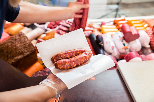 Sales woman in butchery holding sausage wrapped in paper, close-up