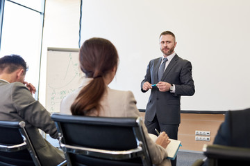 Portrait of bearded business coach standing by whiteboard giving presentation for audience, copy...