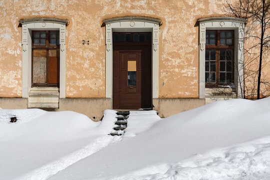 Casa vieja con ventanas tapadas y rellano con nieve