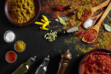 Set of indian spices on black background - green cardamom, turmeric powder, coriander seeds, cumin, and chili, top view