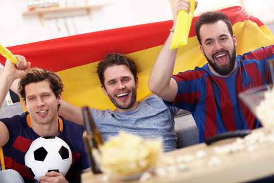 Happy male friends cheering and watching sports on tv