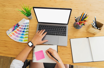 Male designer using laptop at creative studio desk, top view.	
