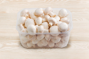 White button mushrooms in the plastic container on wooden surface