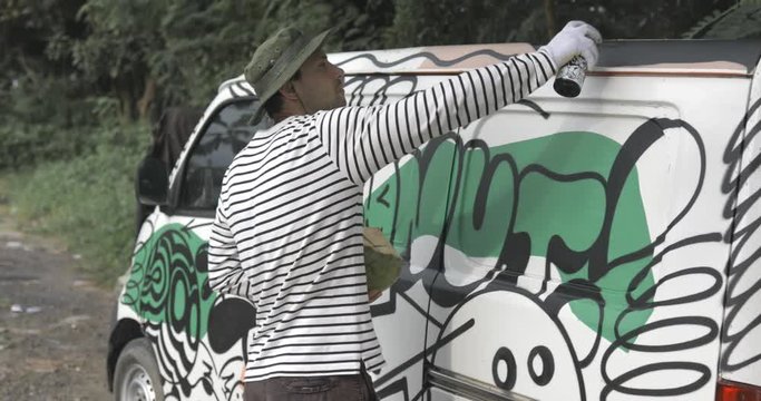Young guy draw graffiti on the car body . The process of drawing color graffiti on a car with aerosol cans