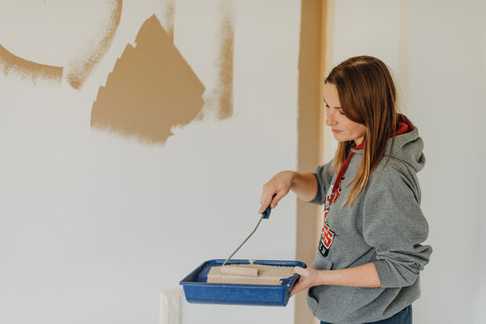 young woman painting wall with a roller and holding paint tray