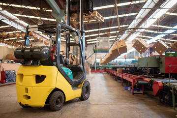 The forklift is in a large and light warehouse. Yellow color