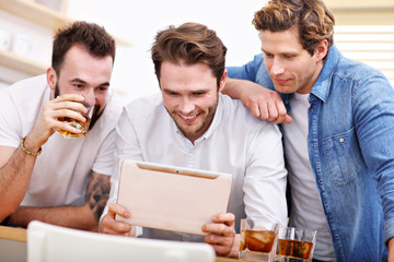 Cheerful friends having fun with smartphone and drinking at home