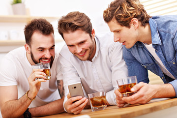 Cheerful friends having fun with smartphone and drinking at home