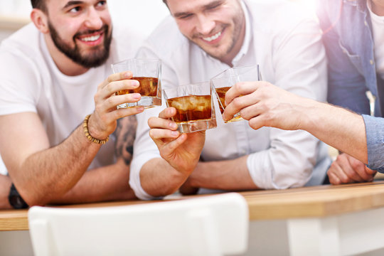 Cheerful friends having fun with smartphone and drinking at home