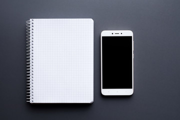 blank white notebook with smartphone over grey desktop