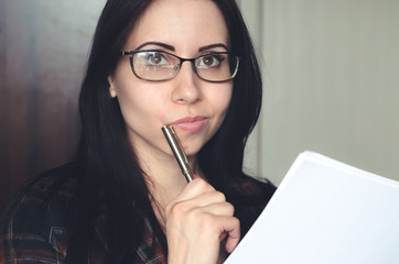 Young caucasian girl with glasses holds a pen and a document and thinks