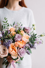Very nice young woman holding big and beautiful colourful flower wedding bouquet with purple carnations and mattiolas, cream David Austin roses, ranunculus and pistachios