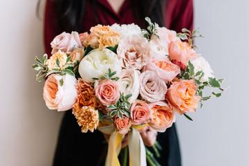 Very nice young woman holding big and beautiful colourful flower wedding bouquet of David Austin roses, ranunculus, peach campanella roses and pistachios