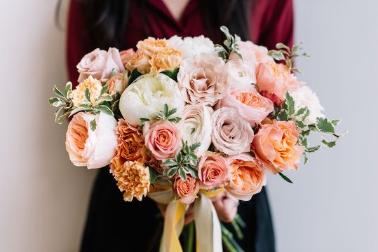 Fototapeta Very nice young woman holding big and beautiful colourful flower wedding bouquet of David Austin roses, ranunculus, peach campanella roses and pistachios