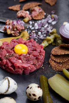Steak tartare, gourmet delicacy raw meat starter. Minced beef dish with onion, mustard, capers and pickles served with quail egg yolk and crackers