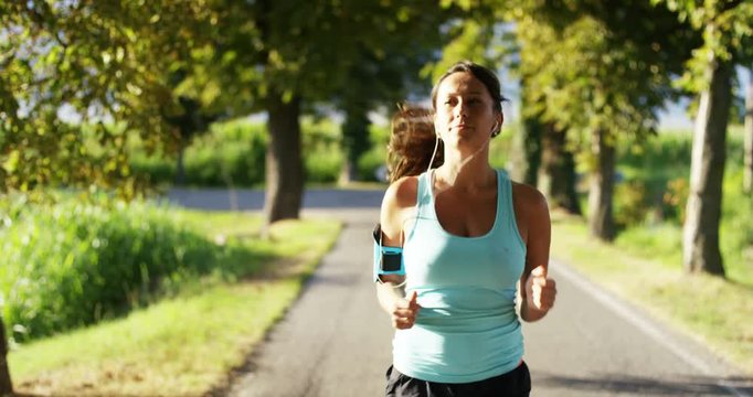 a happy girl fit relaxed jogging and running in a street with trees and nature, using headphones for music and run slow in sunset. concept of happiness for sports and fitness relaxation in nature