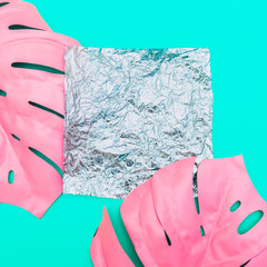metallic holographic square of foil with empty place for text on green background with painted pink  tropical palm leaves. fashion minimal and surreal. flat lay