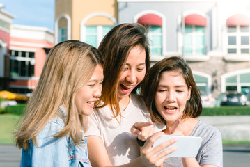 Group of young Asian Women selfie themselves with a phone in a pastel town after shopping. Young women group do outdoor activity under the blue sky. Outdoor activity after shopping concept.
