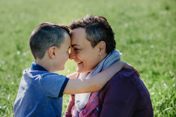 Happy mother and son holding each other nose to nose and smiling outside on shiny day. Happy Mother's Day. Mom of a boy, happy family with small children.