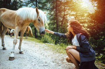 Hübsche junge Frau mit lockigem Haar in der Hocke streichelt ein Pferd im Wald © kay fochtmann