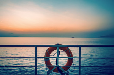 Sunset on the sea and orange lifebuoy at the railing of a cruise ship deck