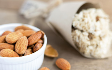 Almonds in a white ceramic bowl with flower bouquet on the wooden table.