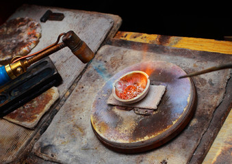 Fototapeta na wymiar The work of jewellery maker. Melting pieces of gold with a gasoline burner.