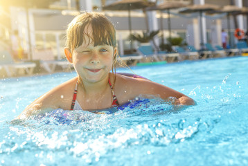 Smiling Little girl winks in the pool of resort hotel sun rays in the background
