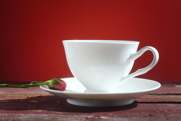 White porcelain Cup with saucer and little rose on red background.