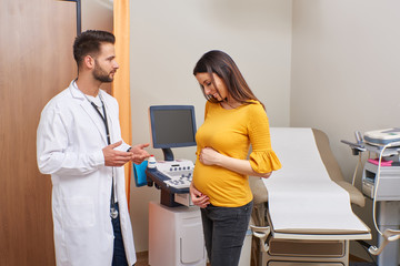 A beautiful young pregnant woman consulting with the handsome doctor in clinic.