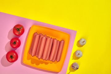 Stack of thin wiener sausages with tomatoes on plate on pink and yellow background