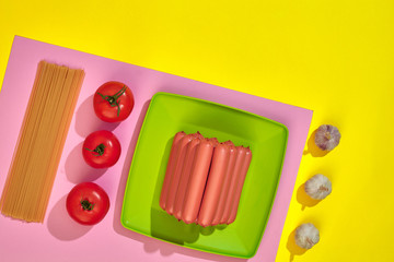 A lot of raw sausages on plate. On yellow background with pasta and vegetables, top view.