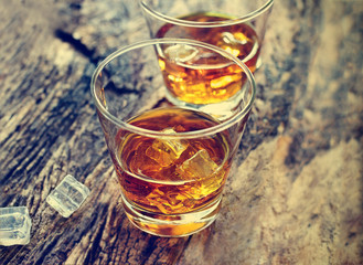 Whiskey bourbon with ice on wooden texture background.
