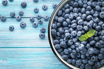 Ripe blueberries in bowl on blue wooden table