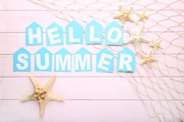 Inscription Hello Summer with starfishes and fishing net on wooden table